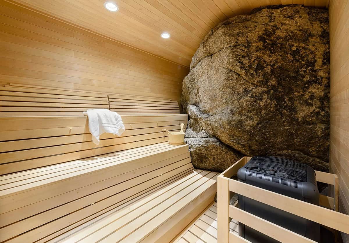 Sauna with wood benches built around a large natural boulder