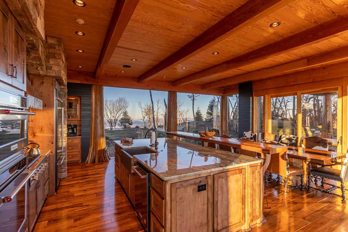 Kitchen island with granite counters overlooks mountains through timber columns