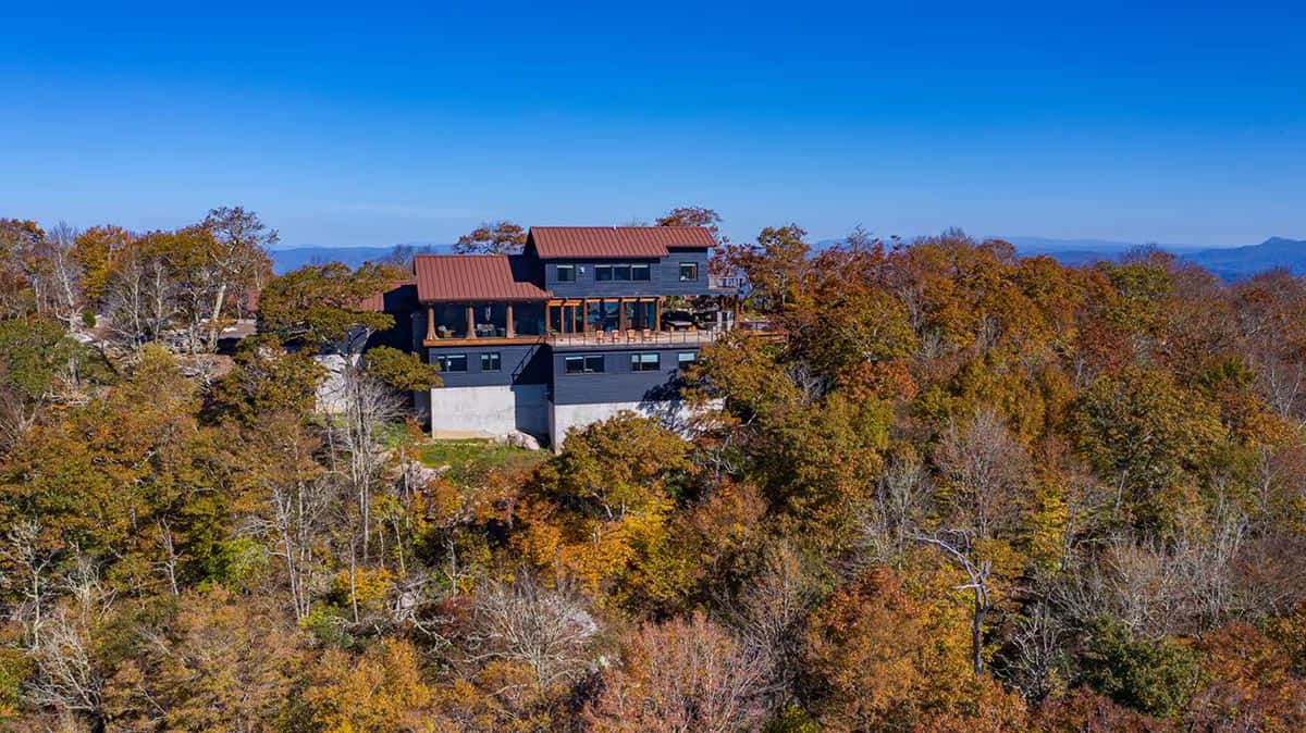 Aerial view of the black timber home atop a forested ridge