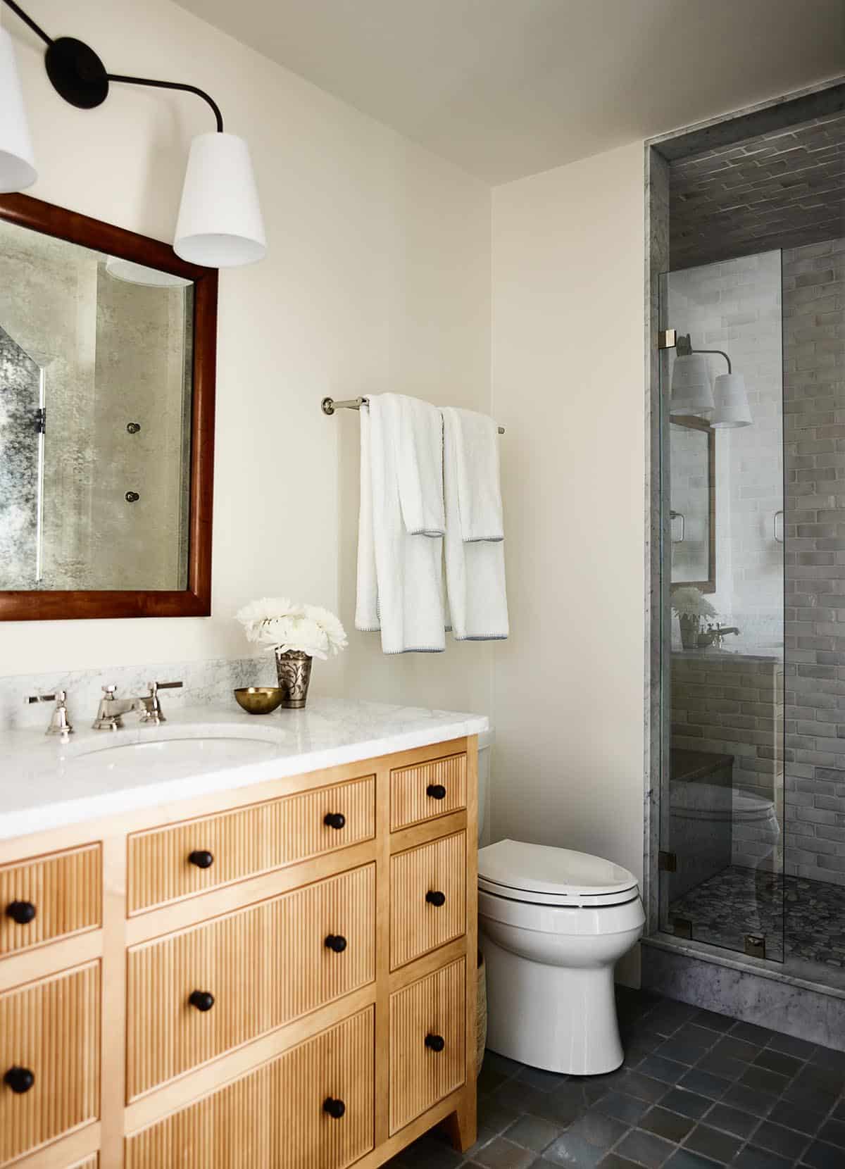 Bathroom with fluted wood vanity, marble countertop, and gray brick tile shower