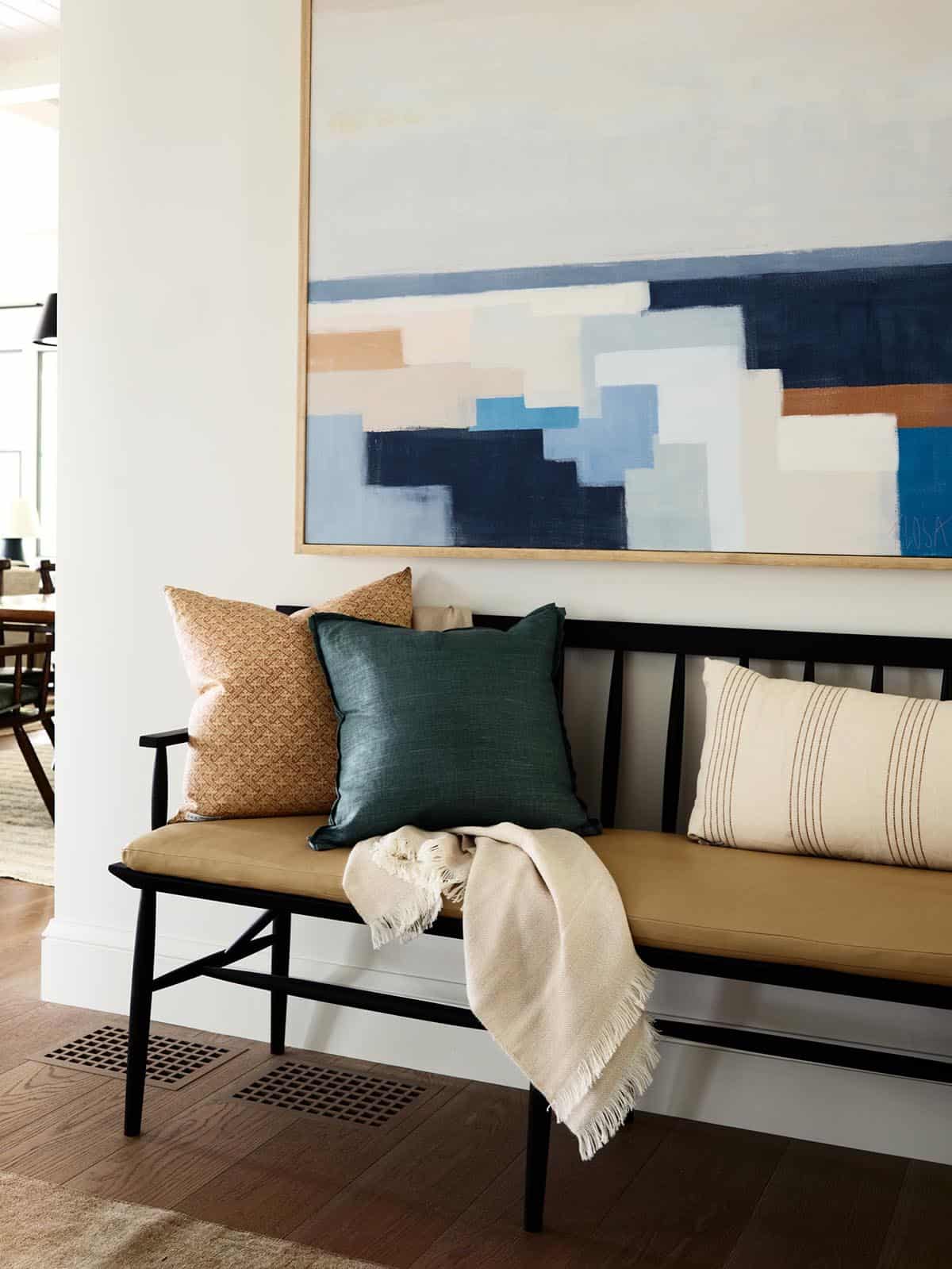 Entry bench with leather cushion, colorful pillows, and abstract coastal artwork