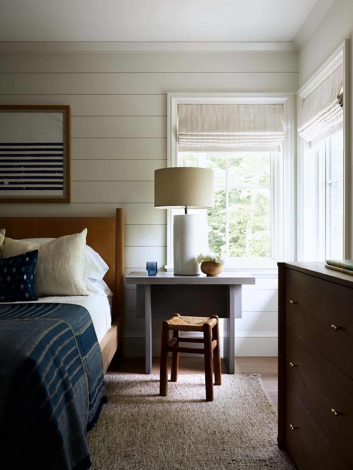 Guest bedroom corner with gray nightstand, woven stool, and shiplap walls