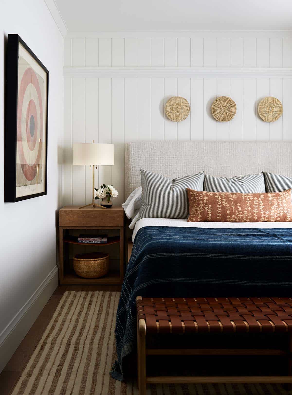 Bedroom with upholstered headboard, woven wall baskets, and leather bench