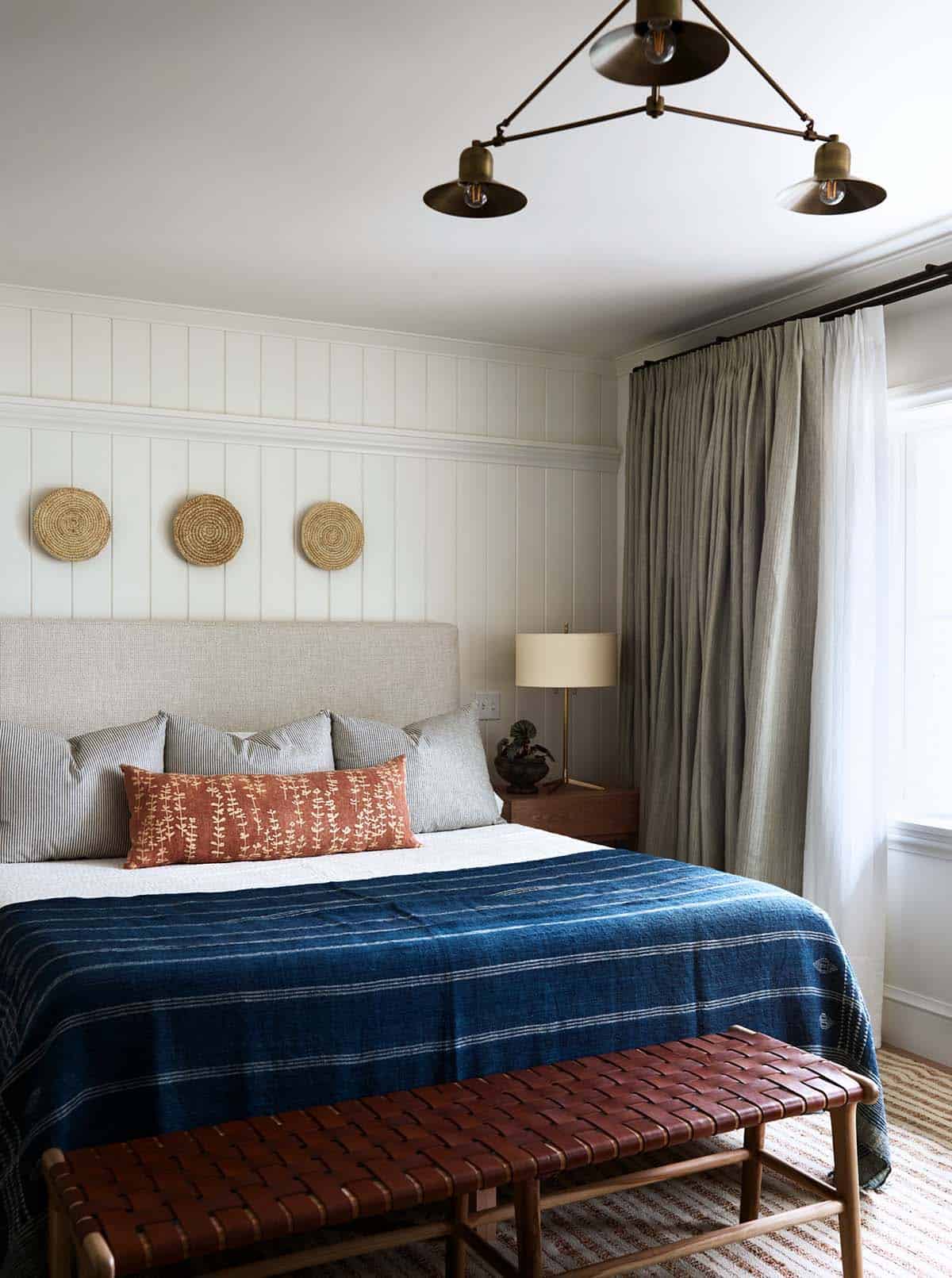 Bedroom with vertical paneling, indigo blanket, and brass triple pendant light