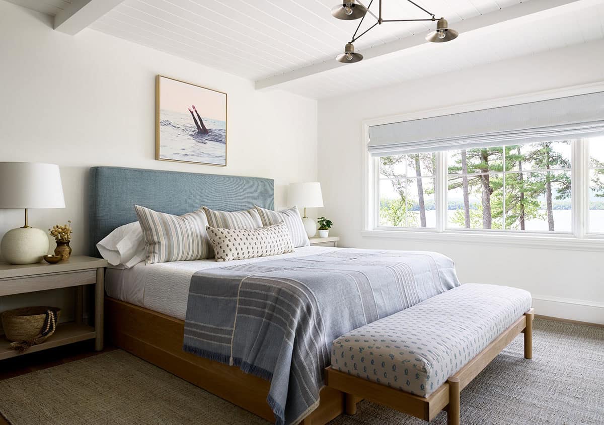 Lake view bedroom with blue headboard, striped throw, and patterned bench