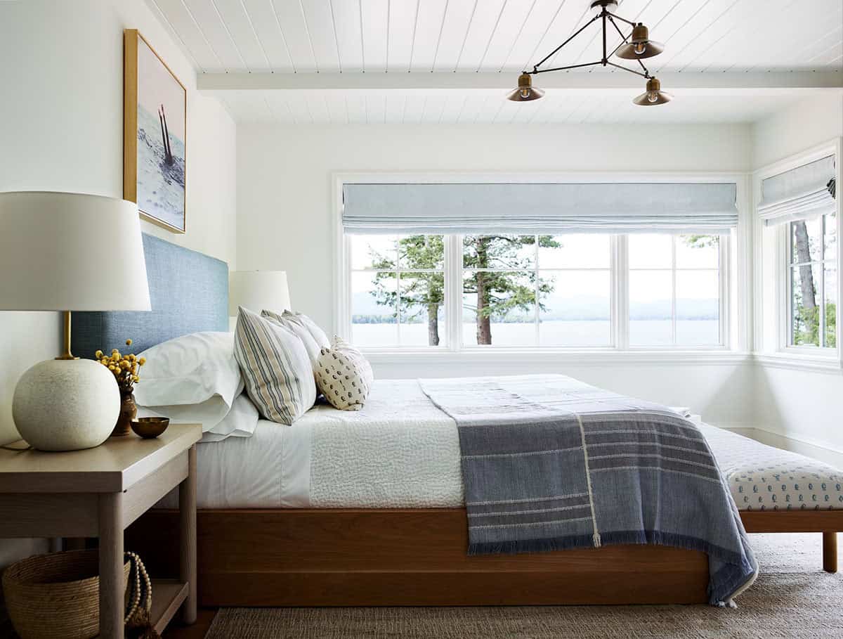 Bedroom with Lake Winnipesaukee views, pine trees, and blue Roman shade