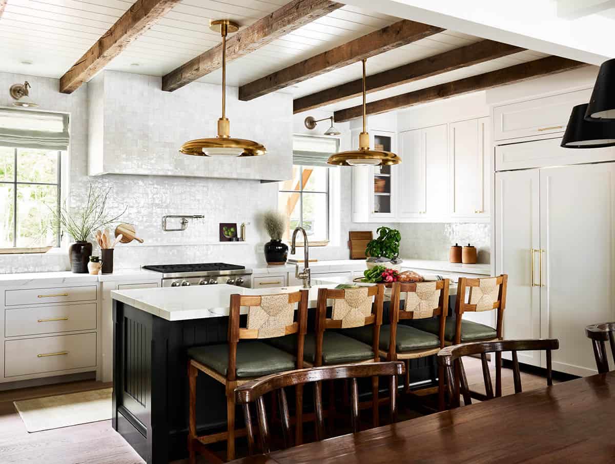 Open kitchen with reclaimed beams, brass pendants, and navy island seating