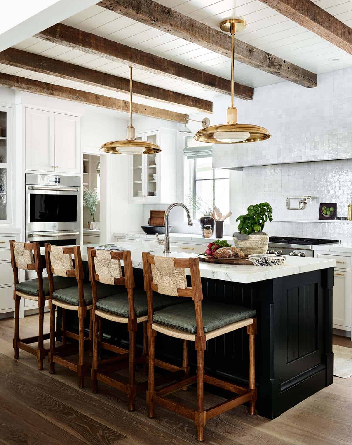 Kitchen island with woven counter stools, brass pendants, and rustic ceiling beams