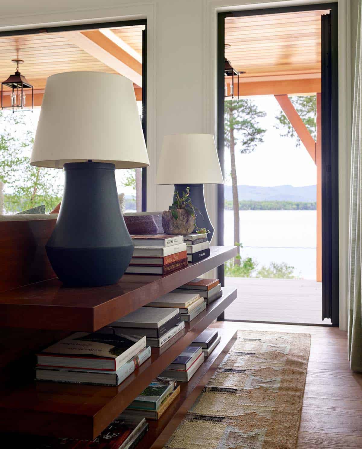 Console table with black lamps, stacked books, and lake view beyond