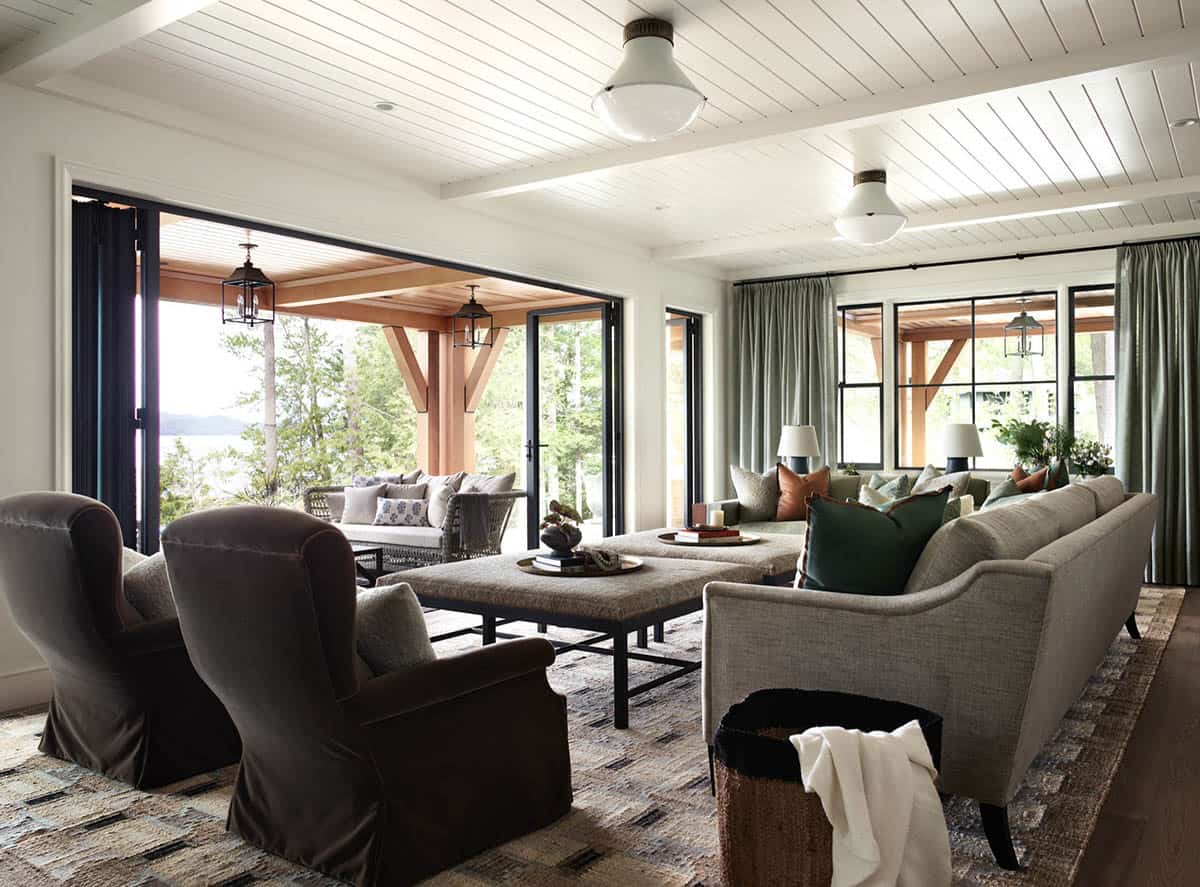 Living room with velvet armchairs, upholstered ottomans, and covered porch beyond