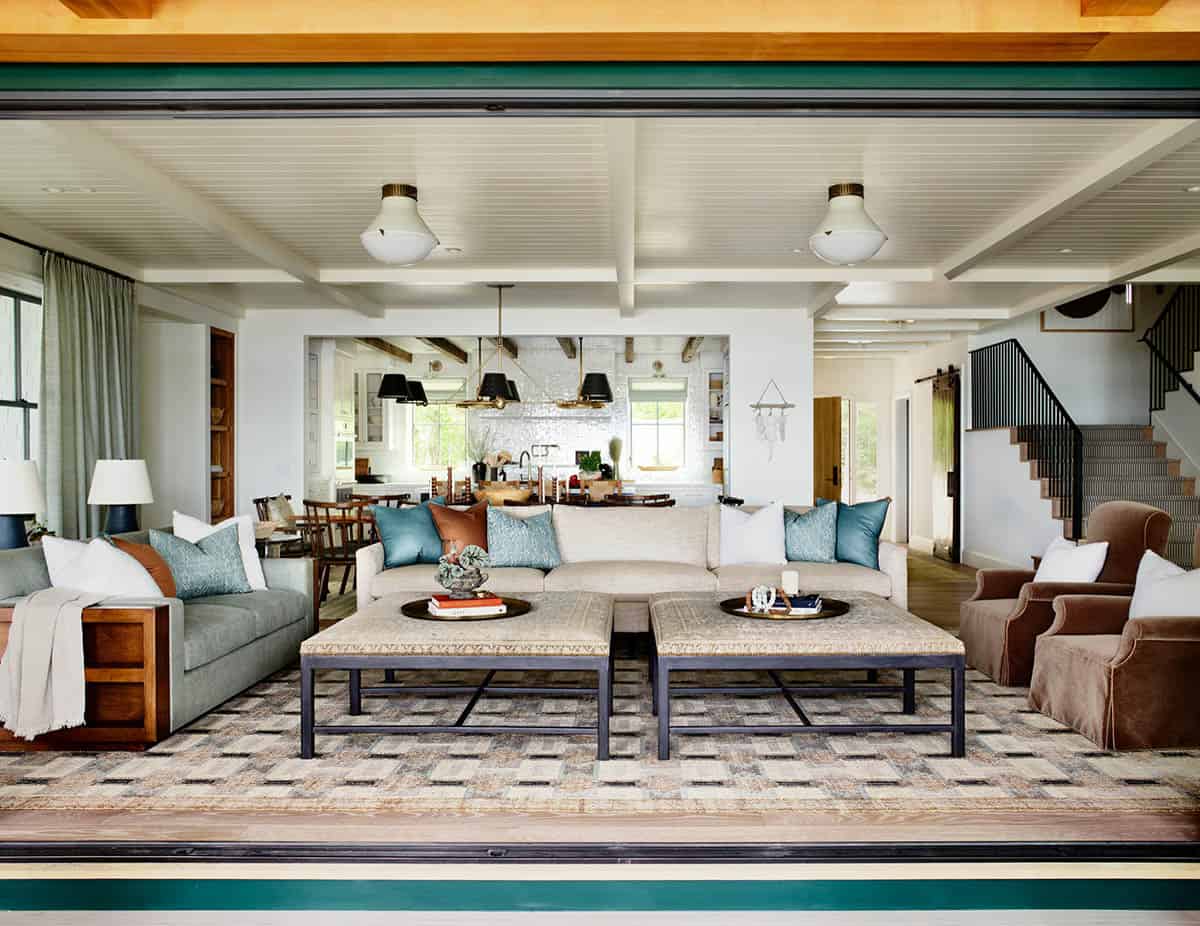 Open living room with kitchen view, tufted ottomans, and stairs beyond