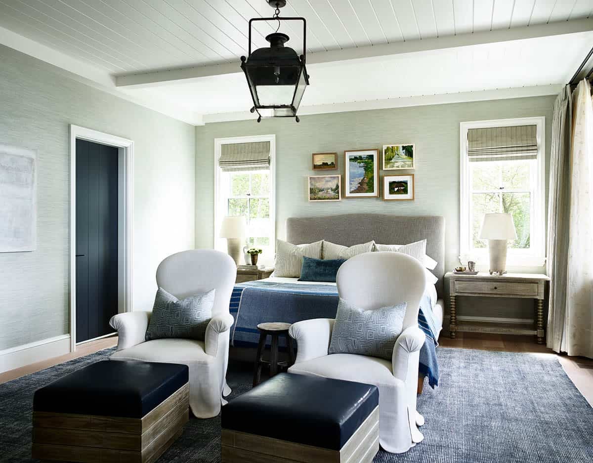 Primary bedroom with gray grasscloth walls, white armchairs, and gallery wall art