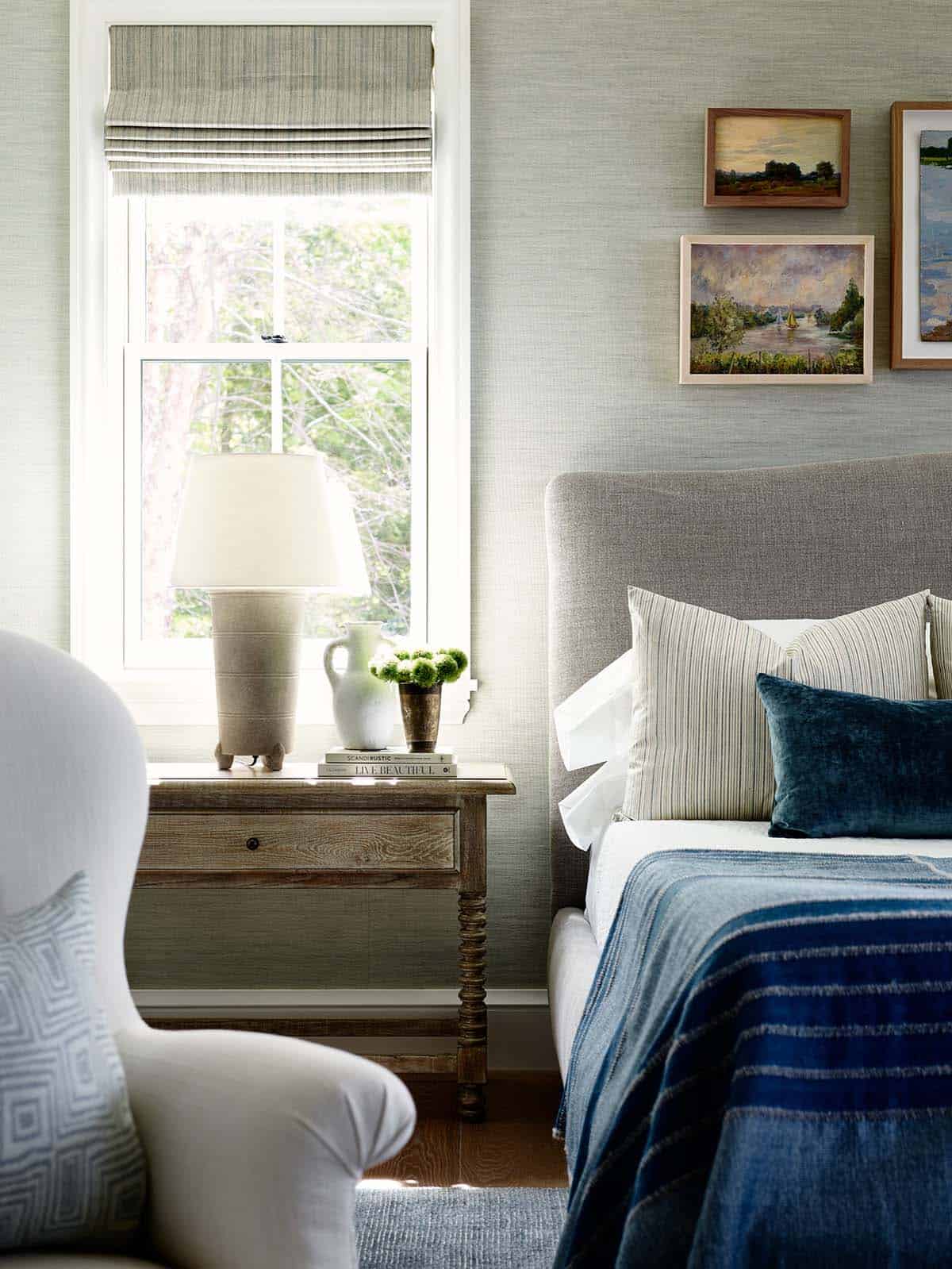 Bedside table with pottery lamp, striped pillows, and framed landscape paintings