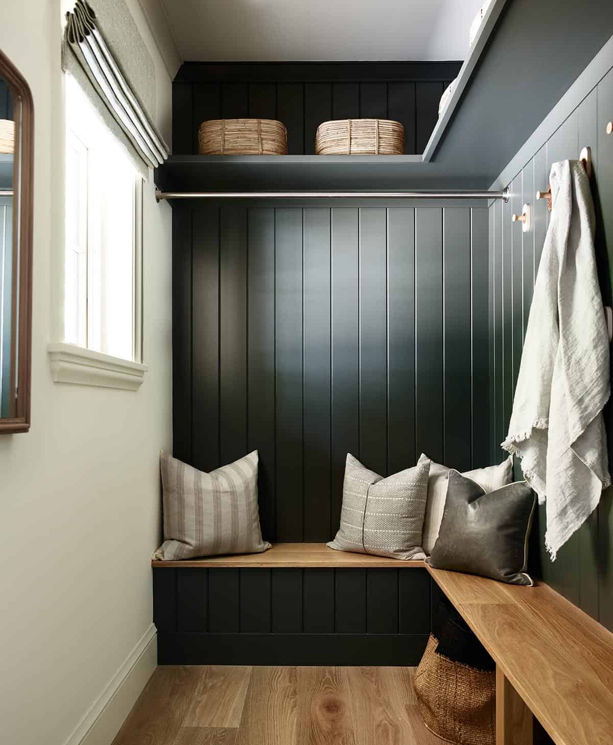 Mudroom nook with dark green paneling, wood bench, and wall hooks