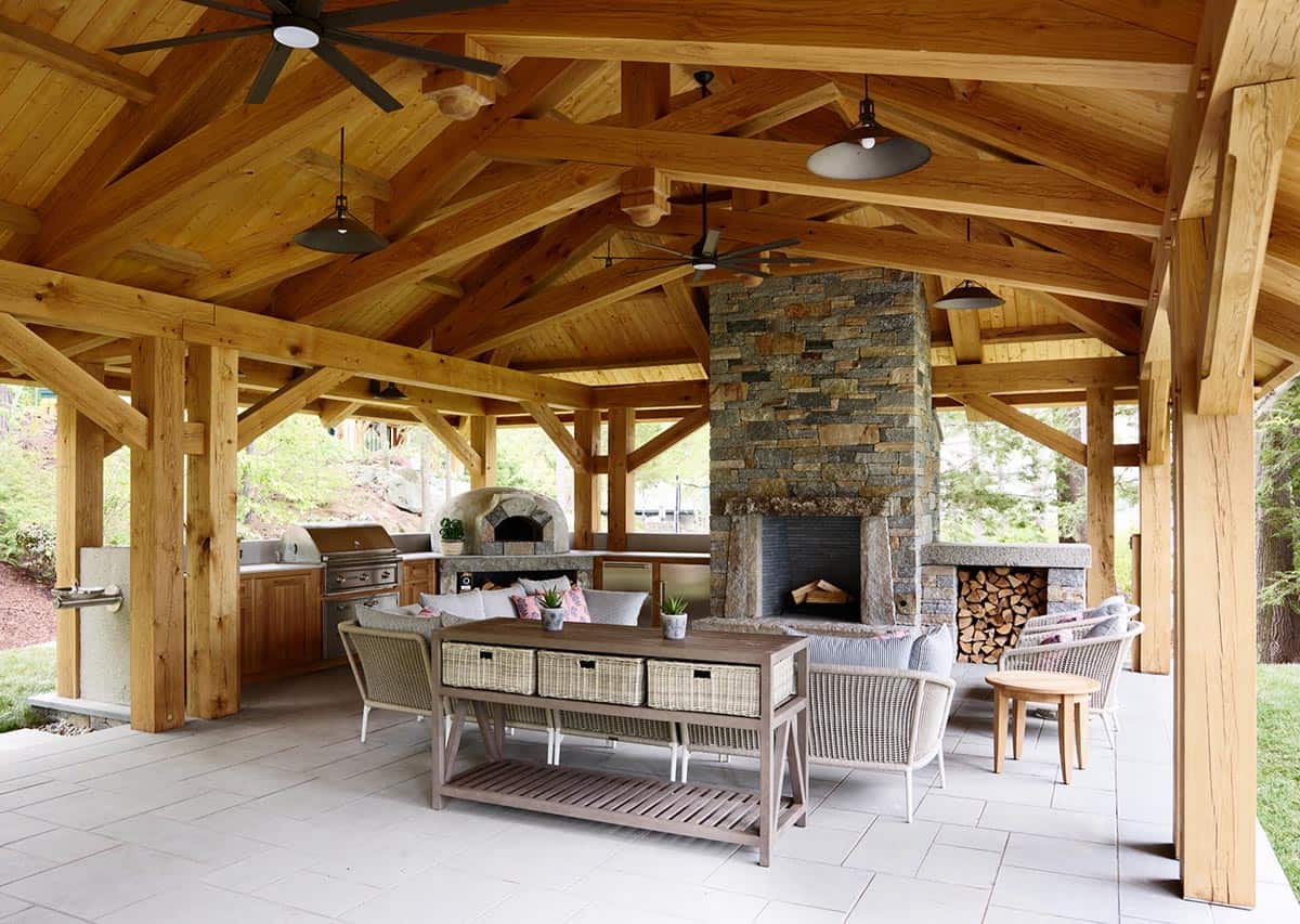 Covered outdoor kitchen with timber trusses, stone fireplace, and pizza oven