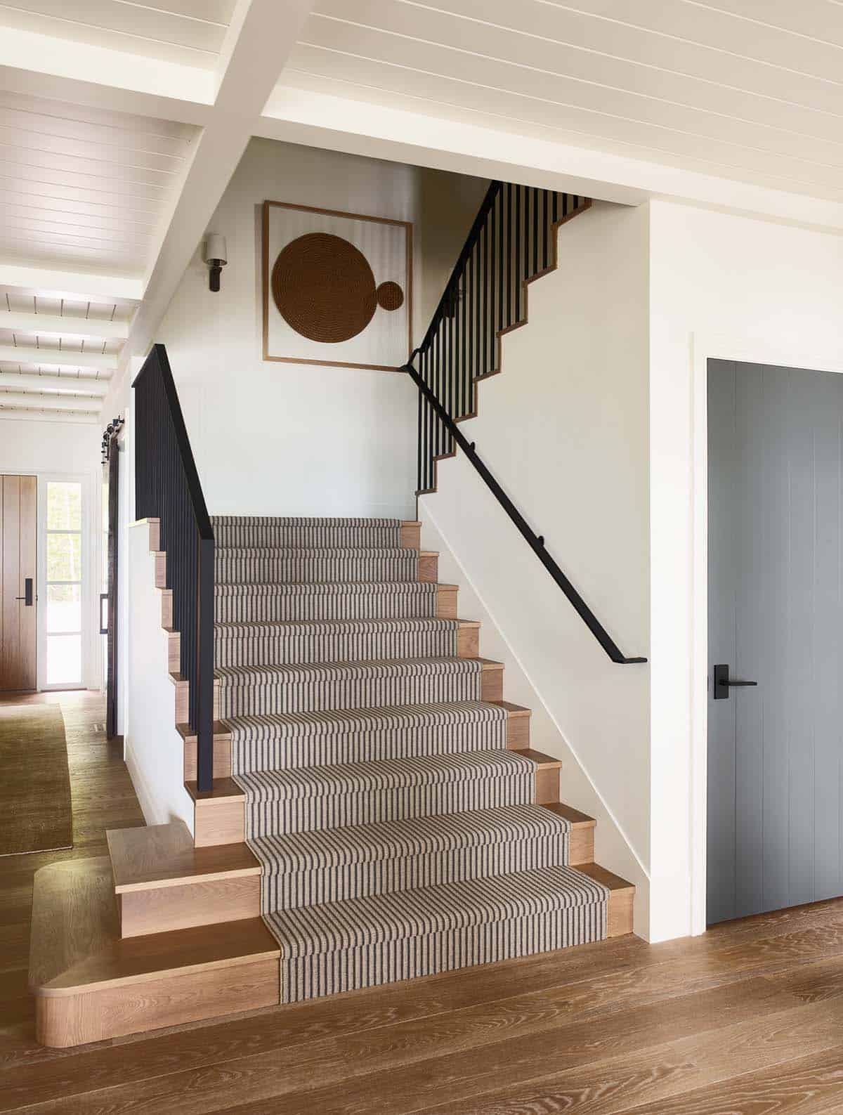 Staircase with striped runner, black railing, and round woven wall art