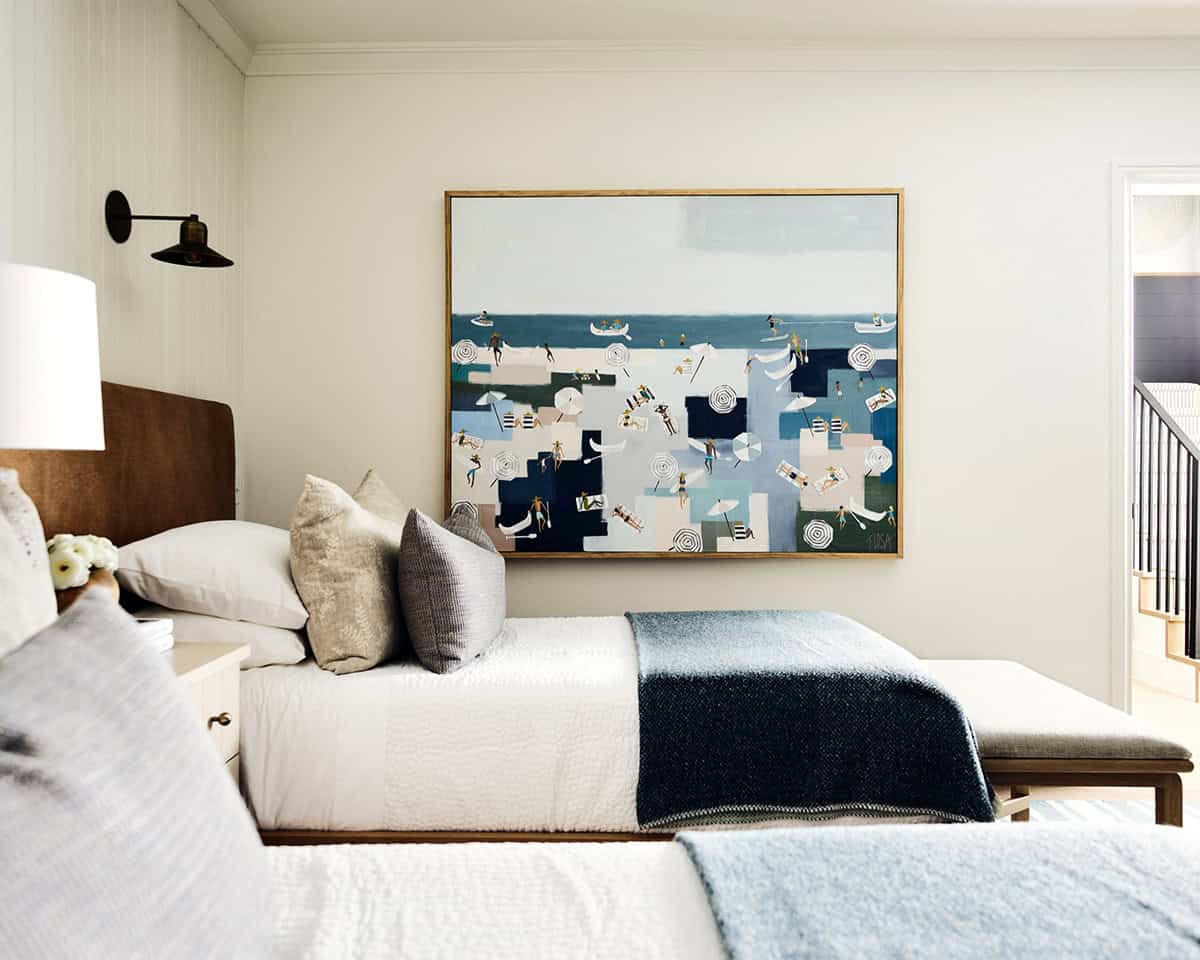 Guest bedroom with beach scene artwork, twin beds, and upholstered bench