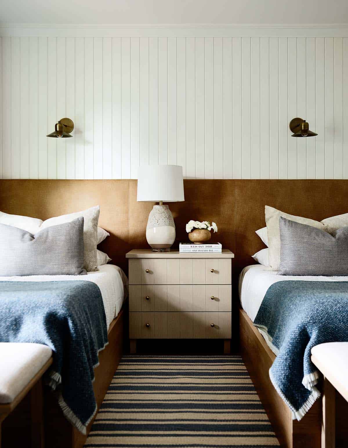 Twin beds with leather headboards, brass sconces, and striped runner between them