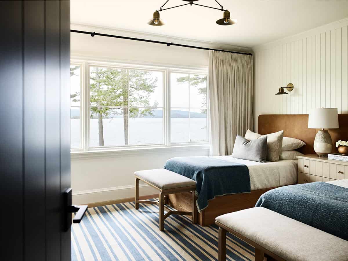 Twin bedroom with striped rug, upholstered benches, and lake views through windows