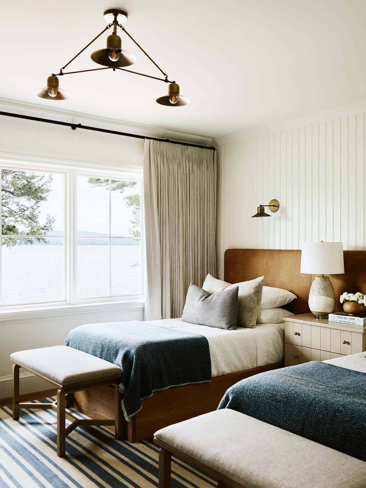 Twin guest bedroom with brass pendant light, blue blankets, and lake view