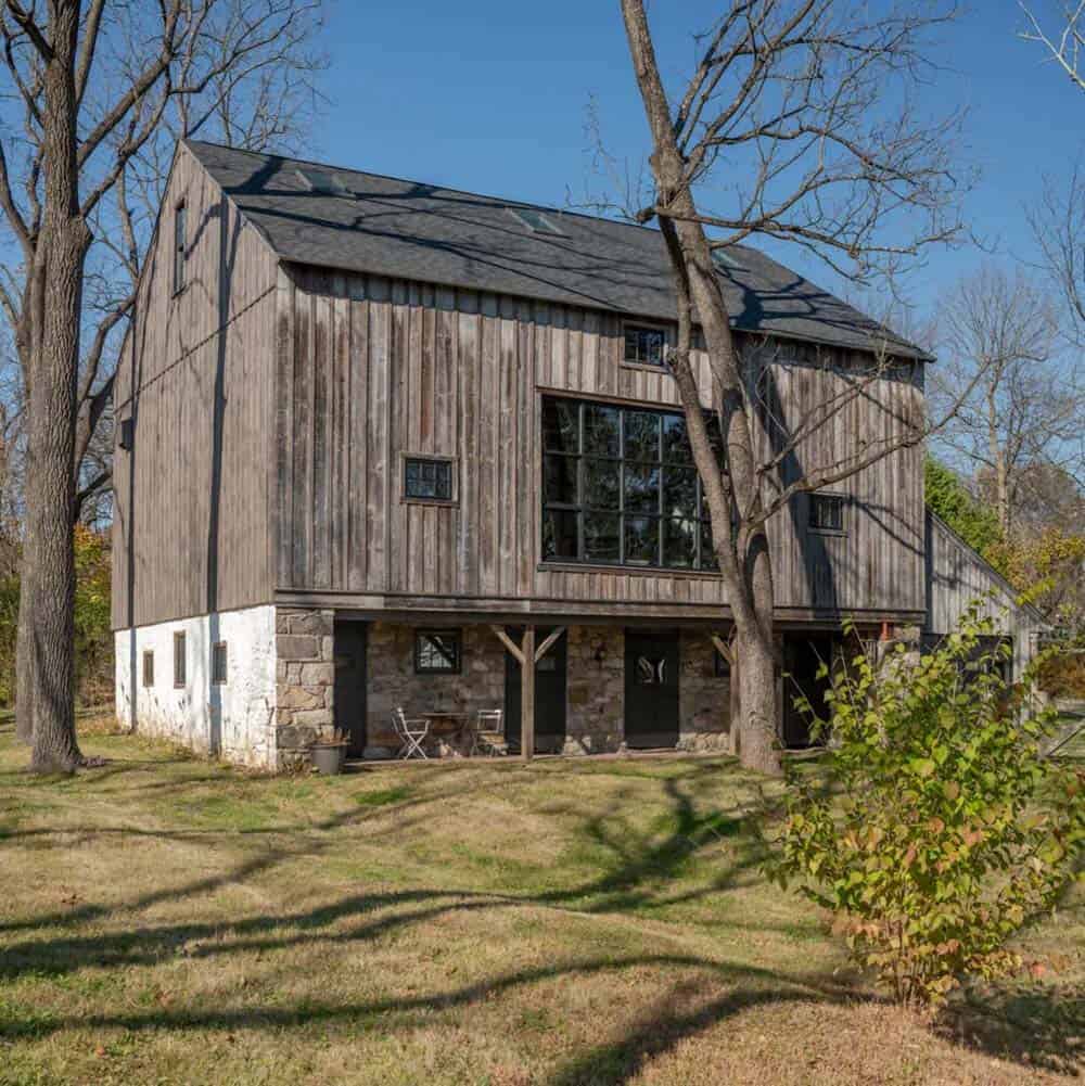Two-story barn exterior showing stone lower level and vertical wood siding above, with a covered porch