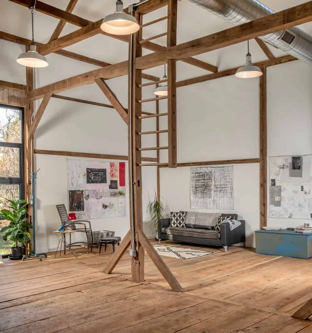Great room with exposed timber framing, wood ladder, wide-plank floors, and modern art on white walls