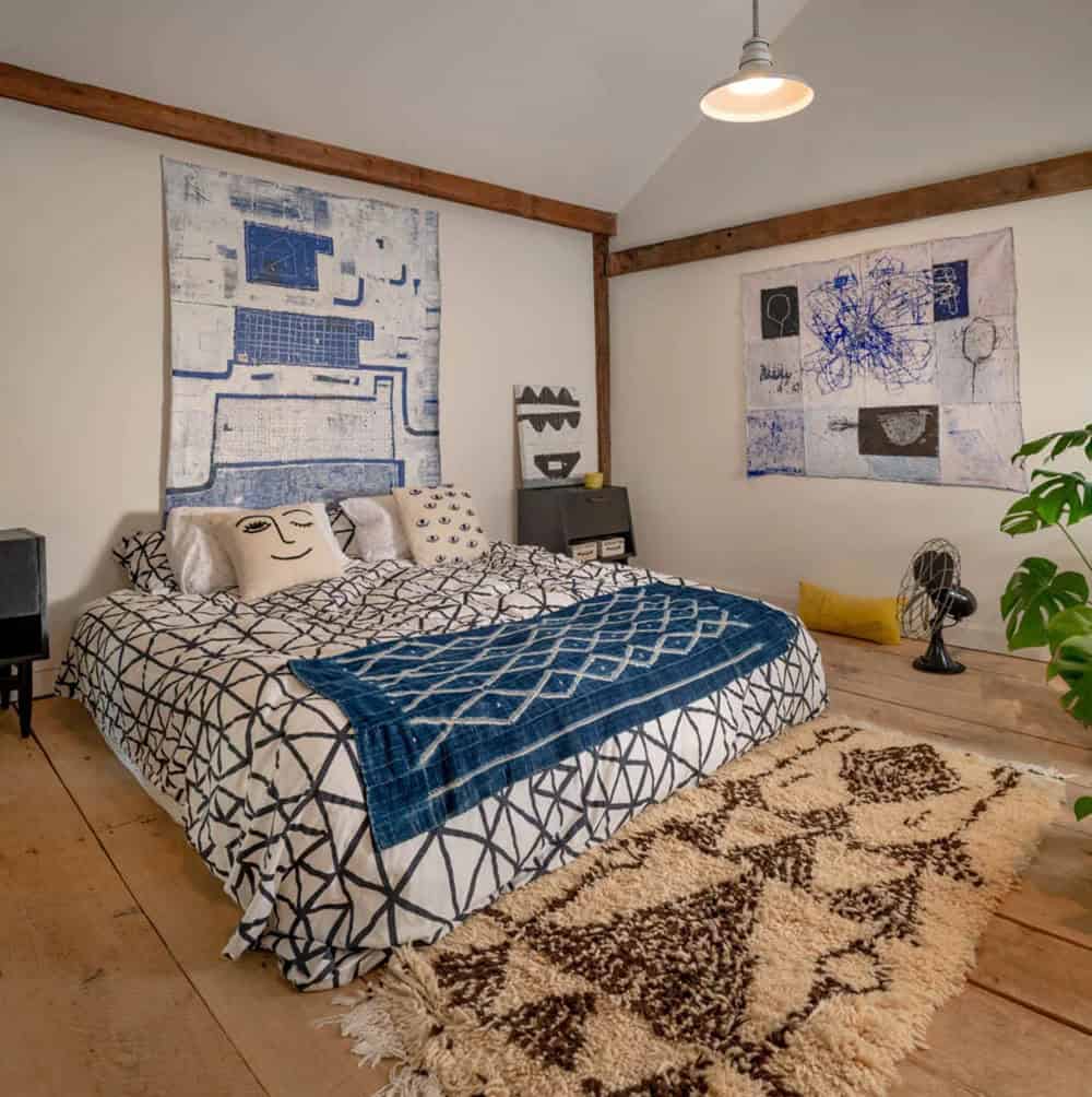 Bedroom with patterned bedding, indigo throw, shag rug, and abstract textile art above the headboard