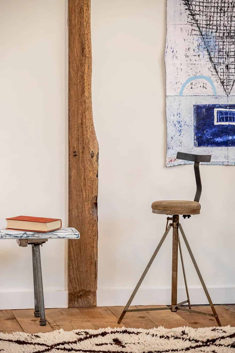 Minimalist vignette with a small stool, industrial swivel chair, and framed artwork against a white wall