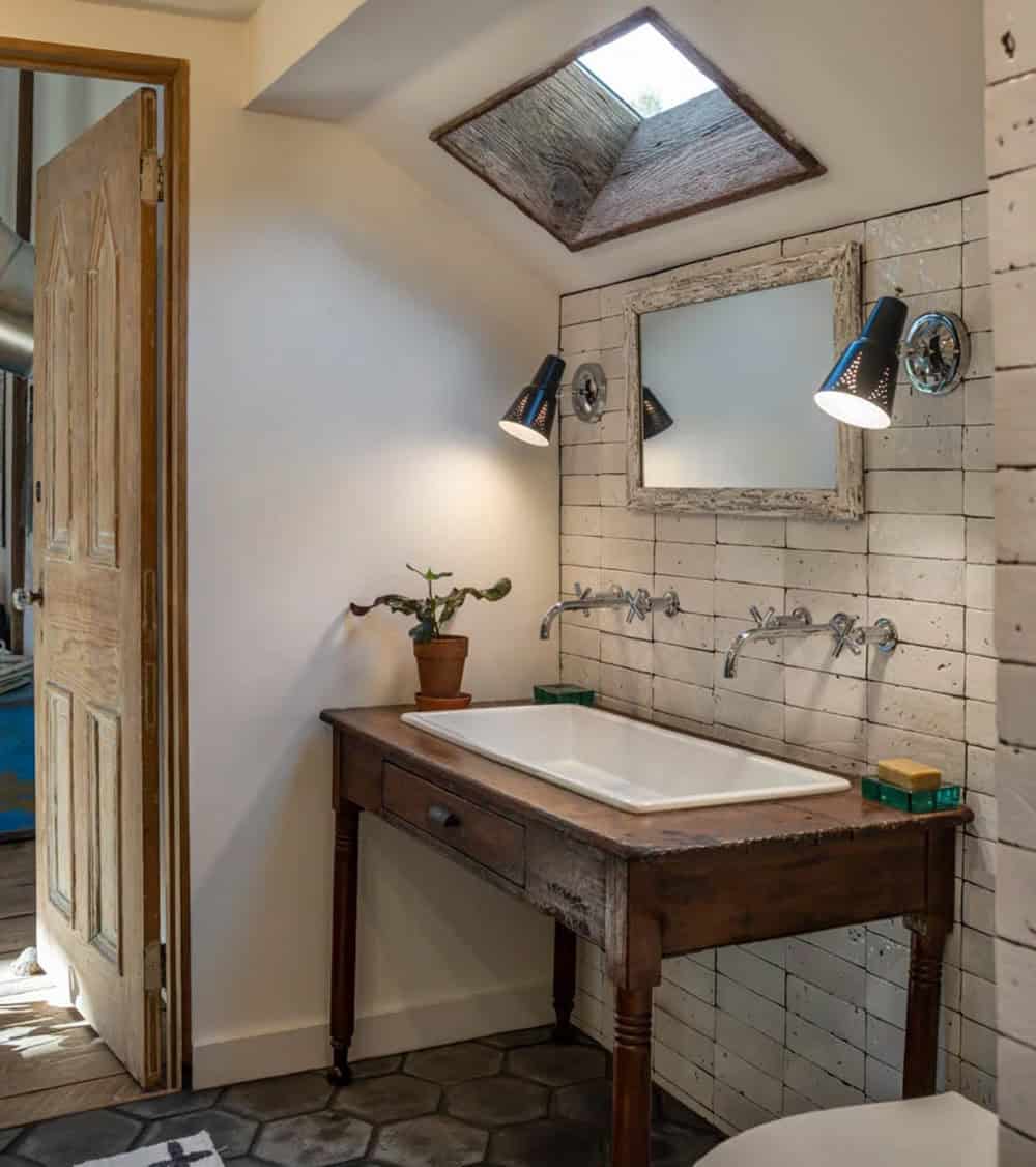 Bathroom vanity made from a vintage wooden table with a farmhouse sink, under a skylight and sconces