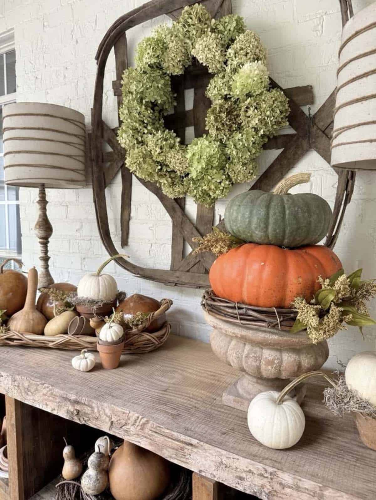 Green hydrangea wreath on vintage tobacco basket above stacked pumpkins in stone urn