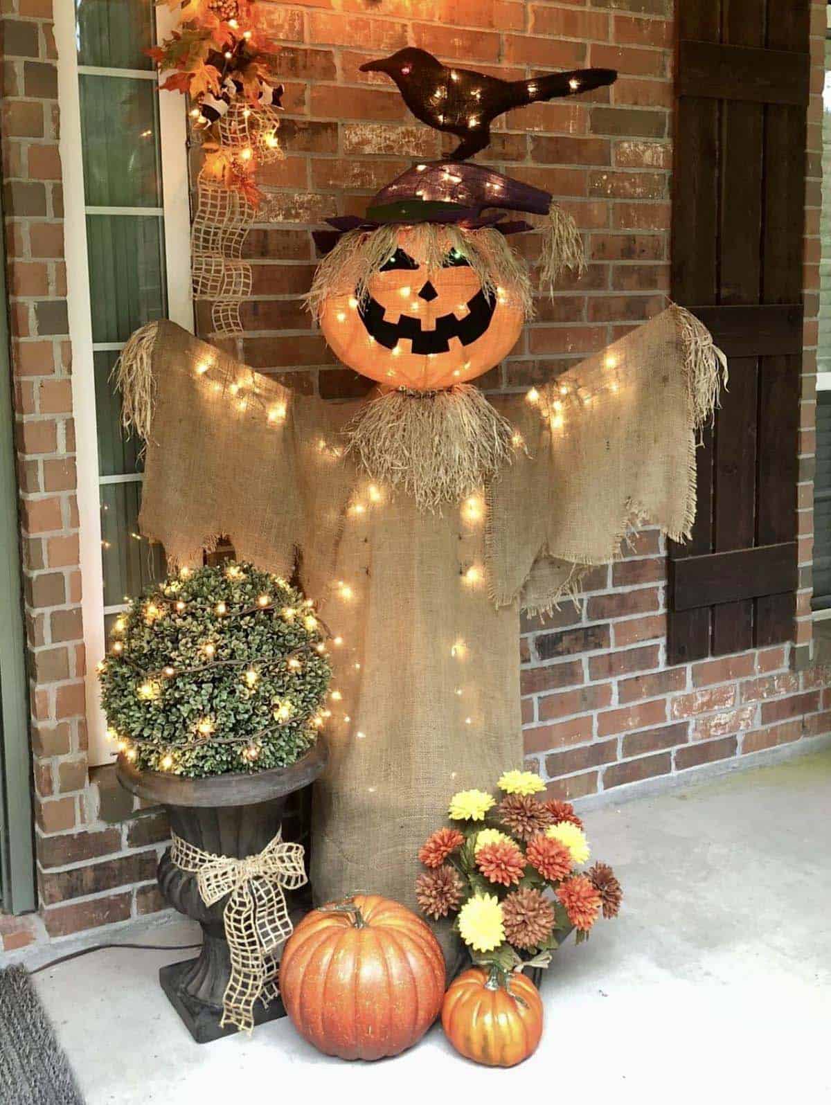 Lit burlap scarecrow with jack-o'-lantern head and crow topper