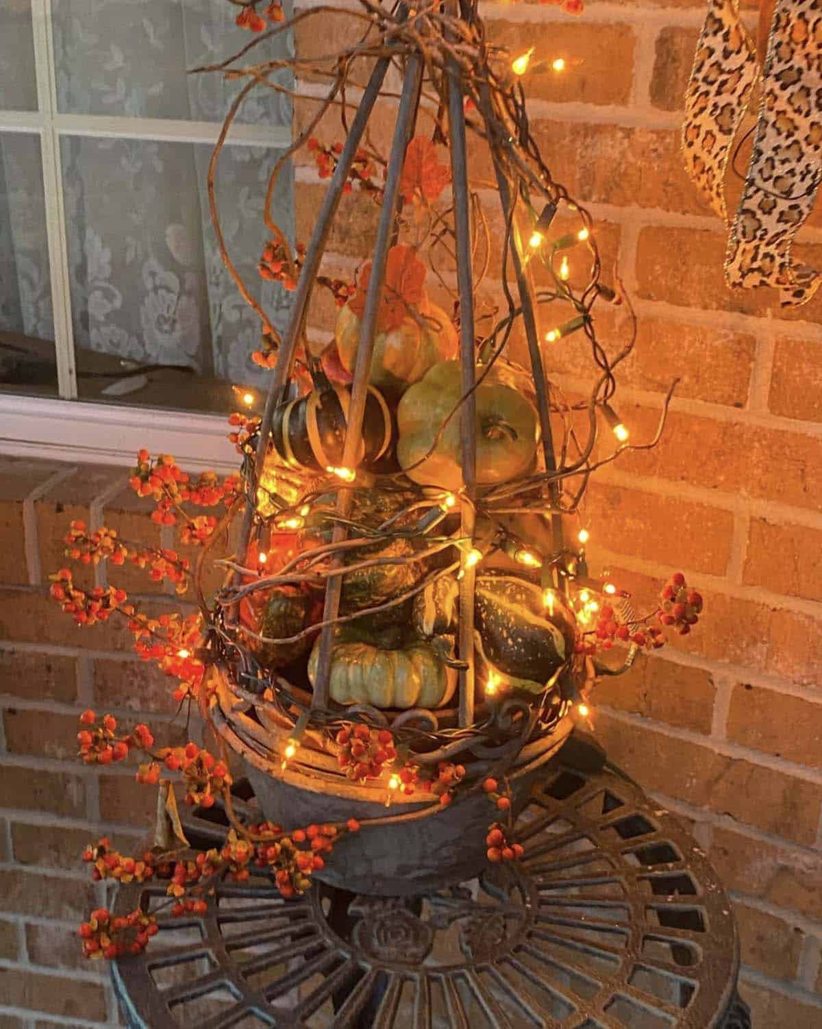 Metal obelisk basket filled with gourds and lit string lights