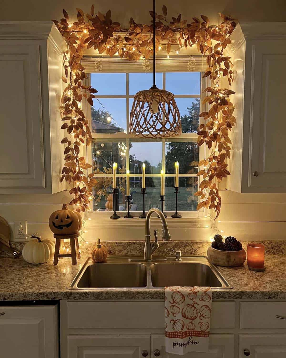 Kitchen window framed with lit leaf garland and taper candles