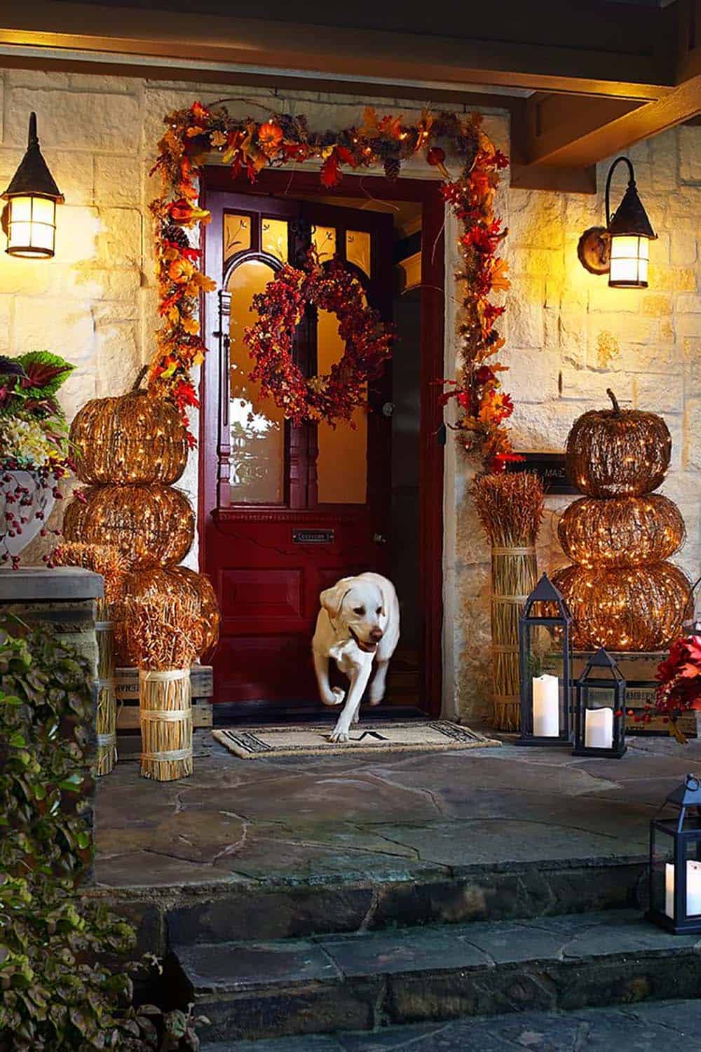 Lit rattan topiary pumpkins flanking a red front door with garland