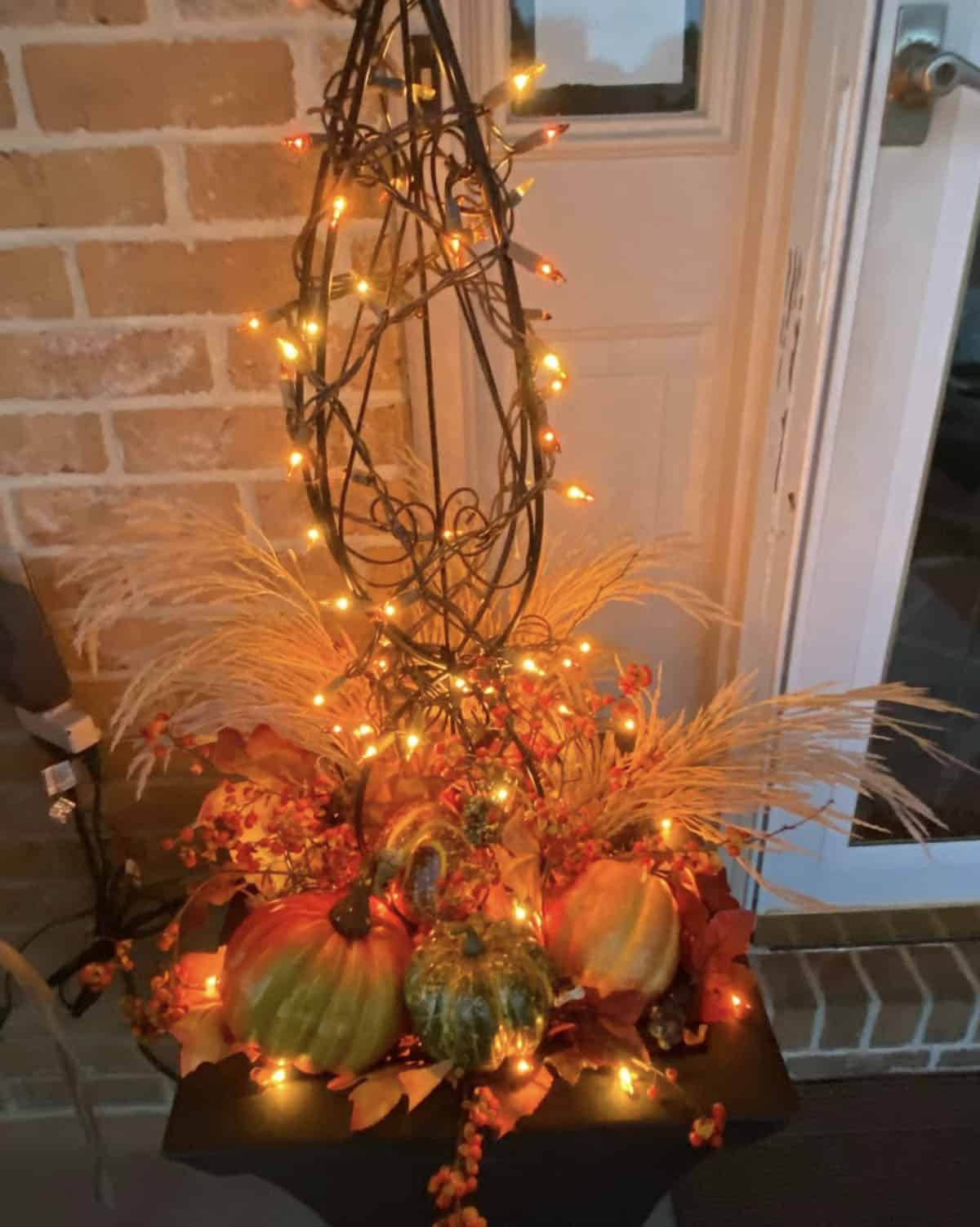 Lit wire topiary with string lights, pumpkins, and pampas grass on the porch