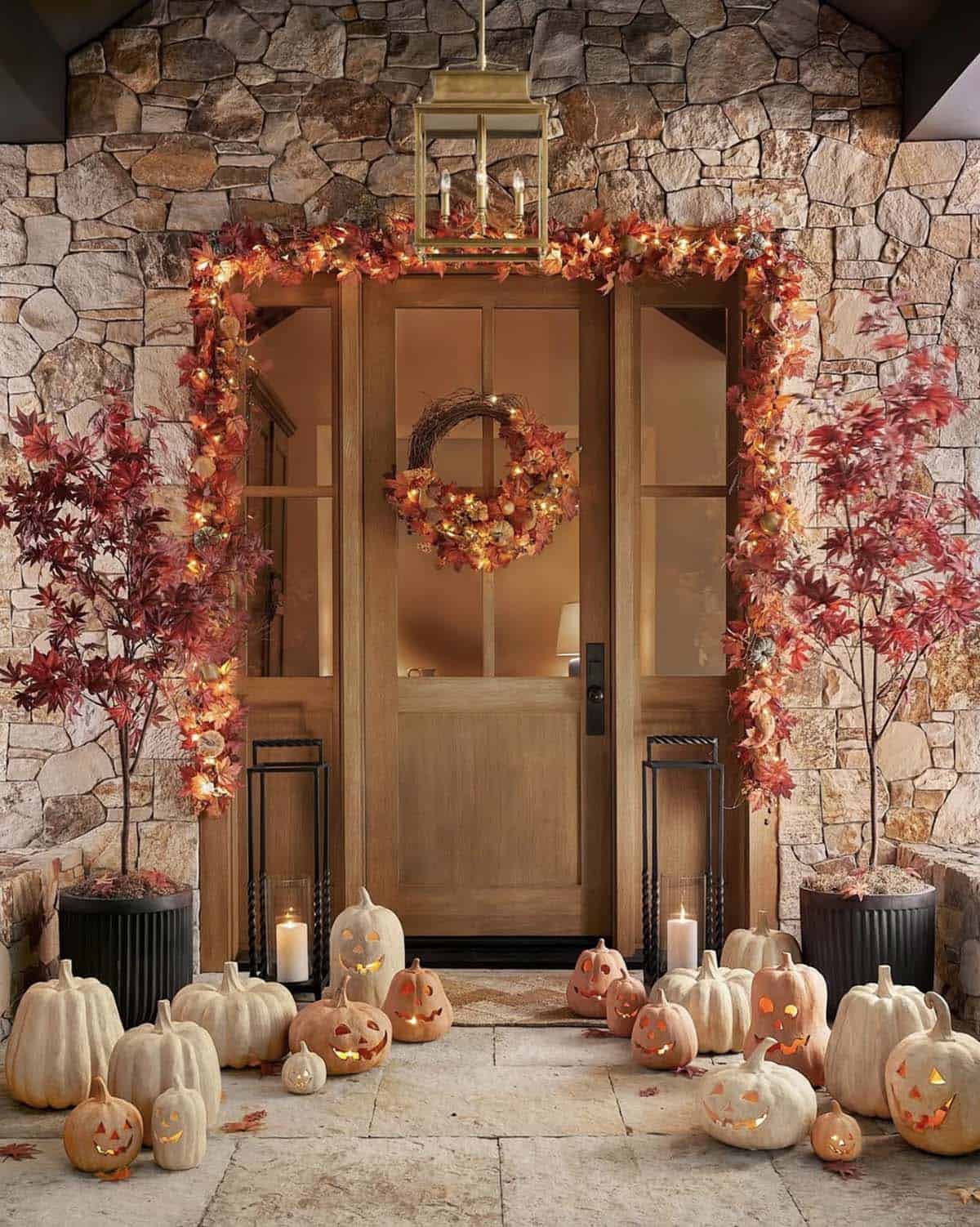 Wooden door framed with a lit garland, wreath and carved pumpkins