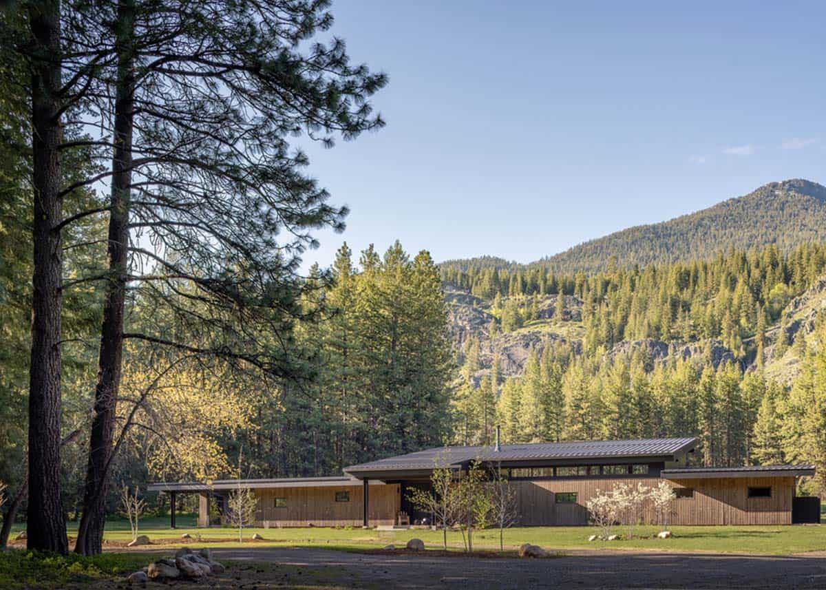 Wide exterior view of shed roof home framed by pines and mountain