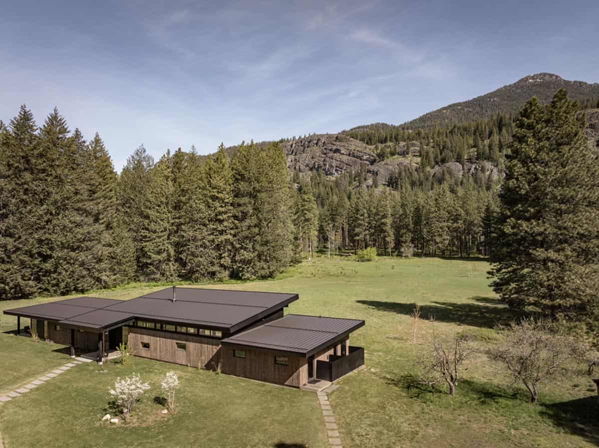 Aerial view of home nestled in open meadow surrounded by forest