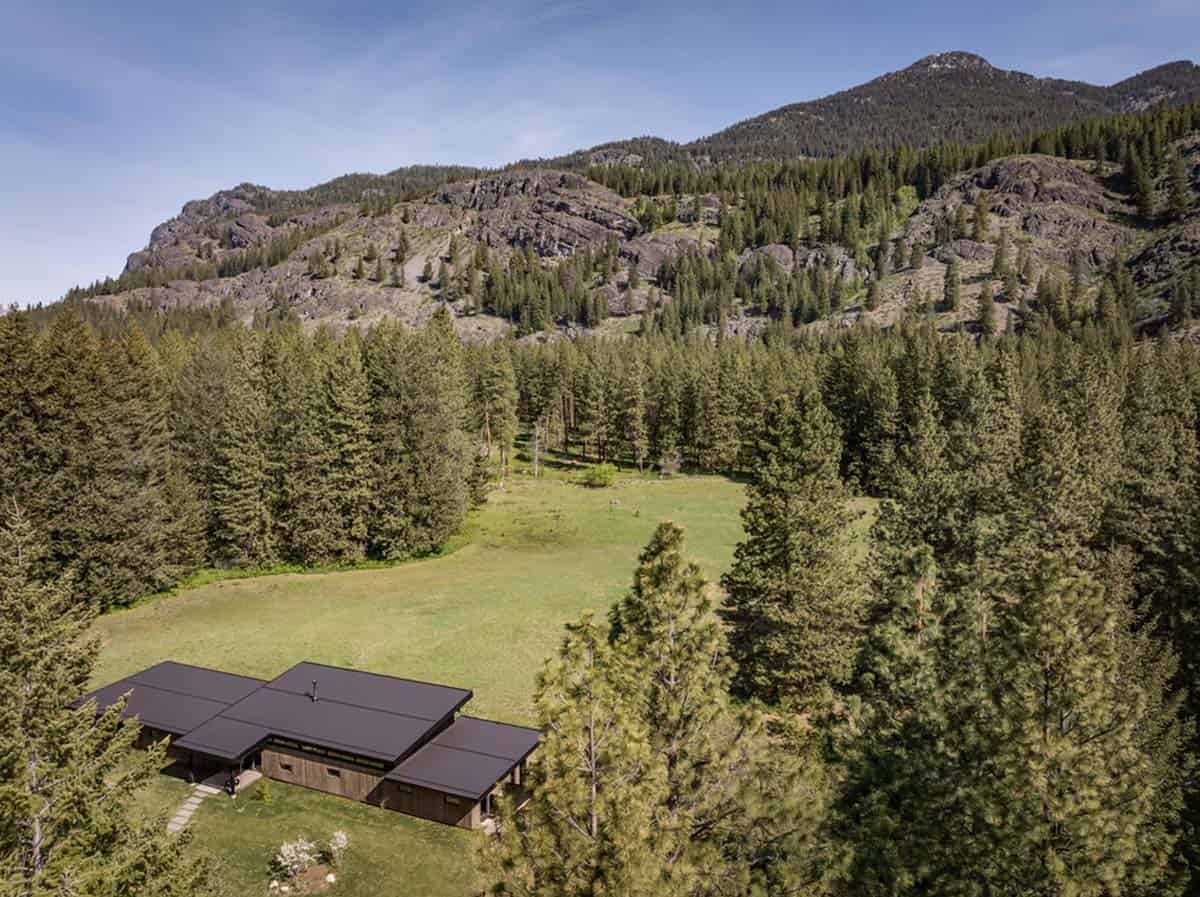 Aerial view of home tucked into meadow below rocky ridge