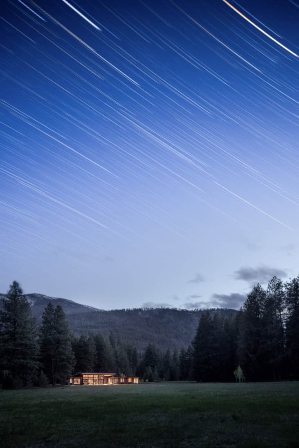 Star trails over meadow home nestled in forest at night