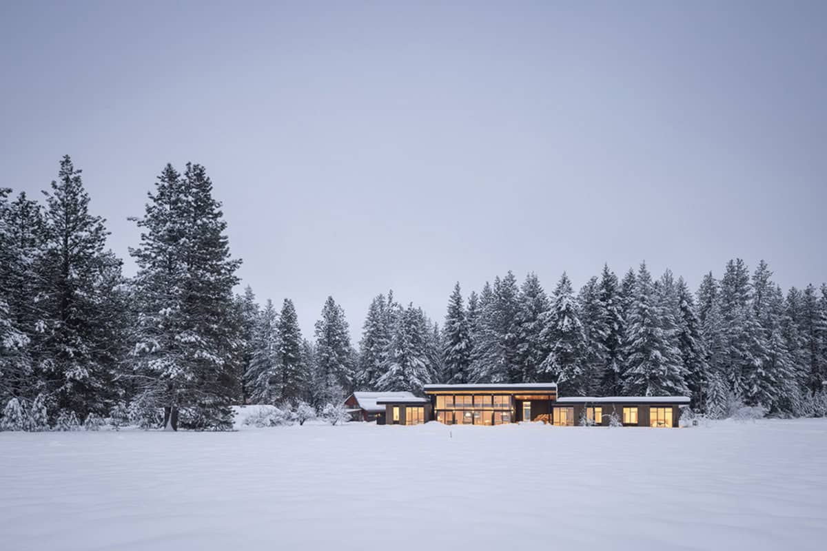 Snow-covered home glowing at dusk surrounded by frosted pines