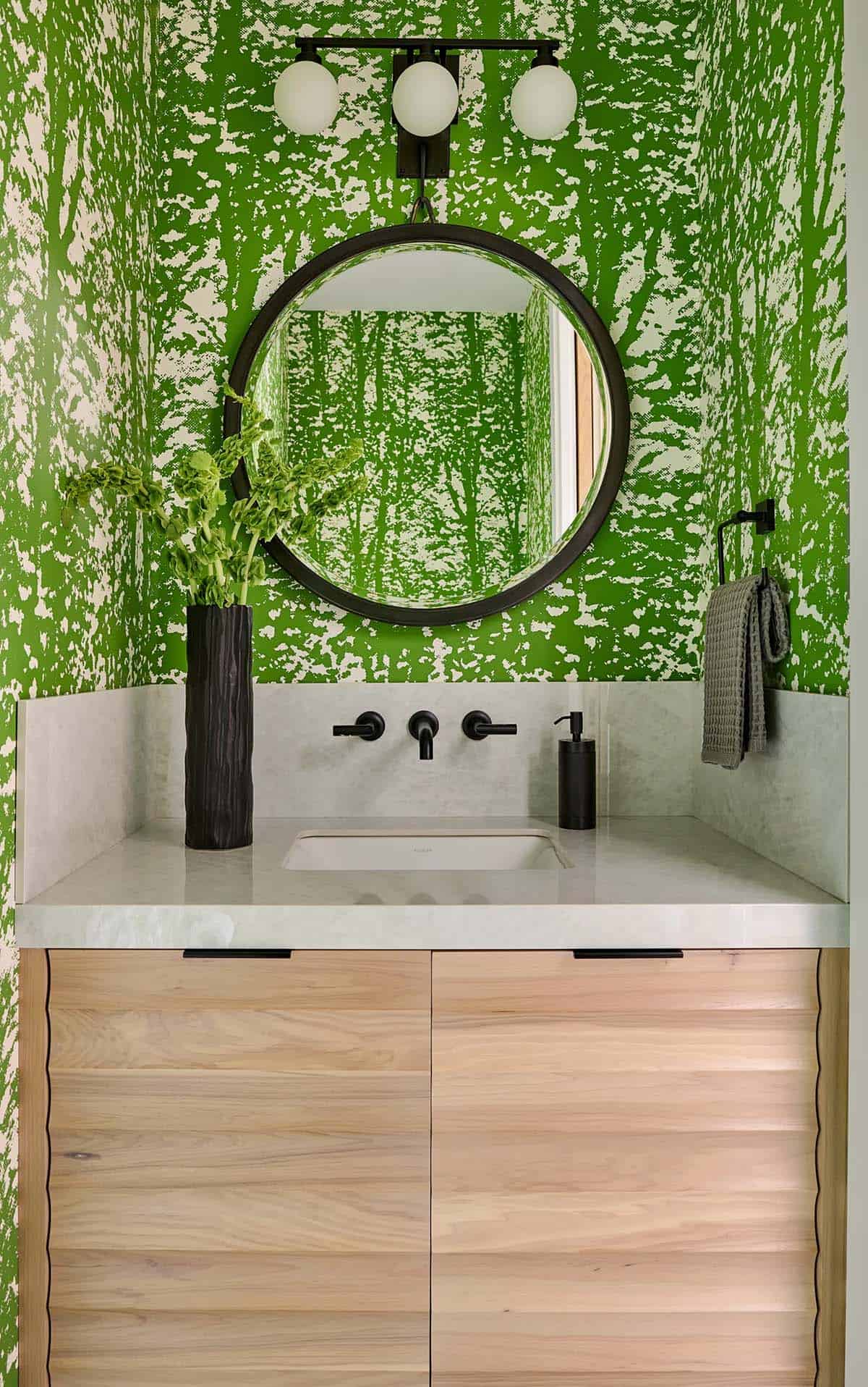 Powder room with bold green wallpaper and round black mirror