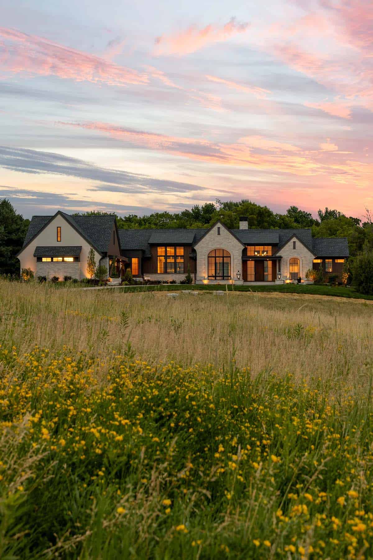 Modern rambler home glowing at sunset behind a yellow wildflower meadow