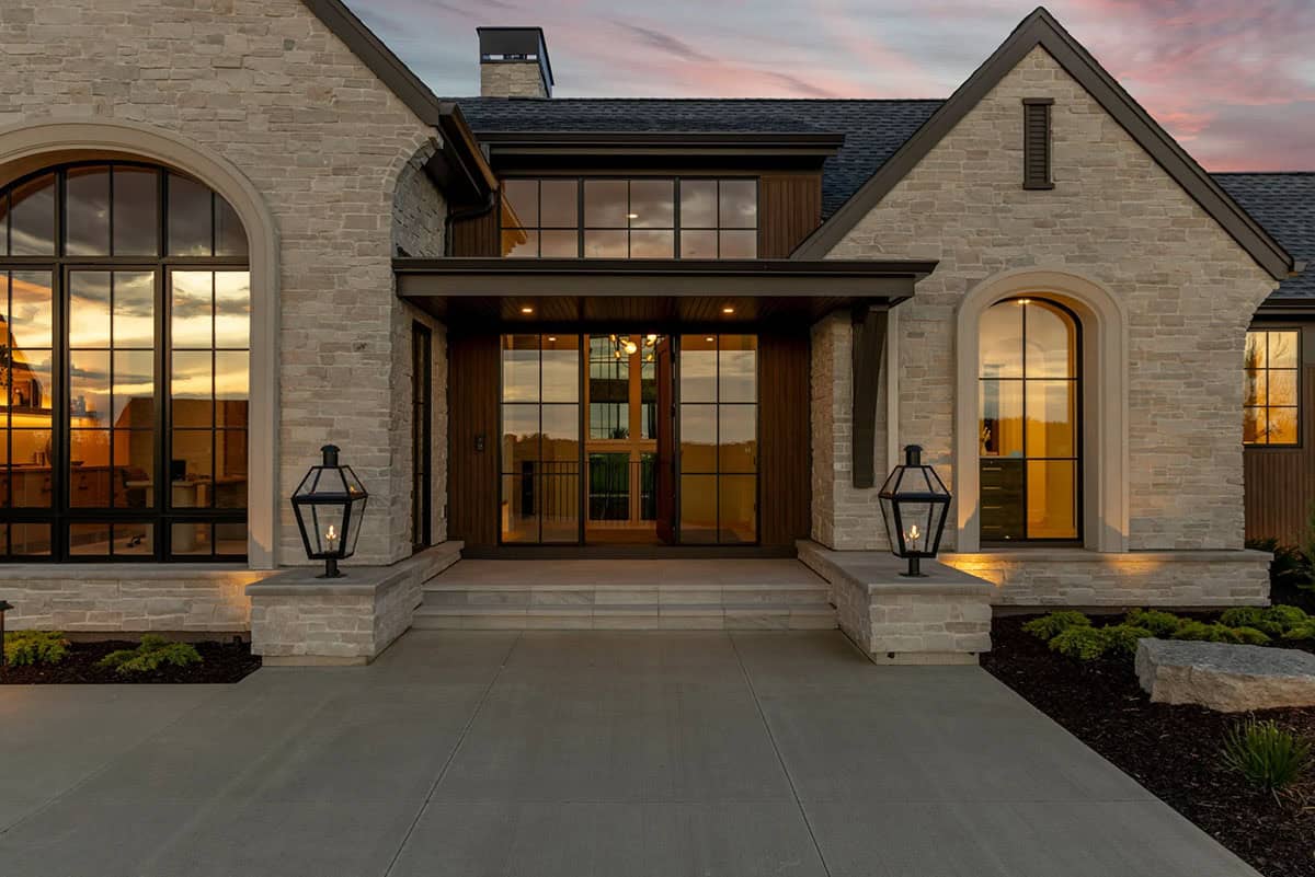 Covered entry with gas lanterns, arched windows, and light stone at dusk
