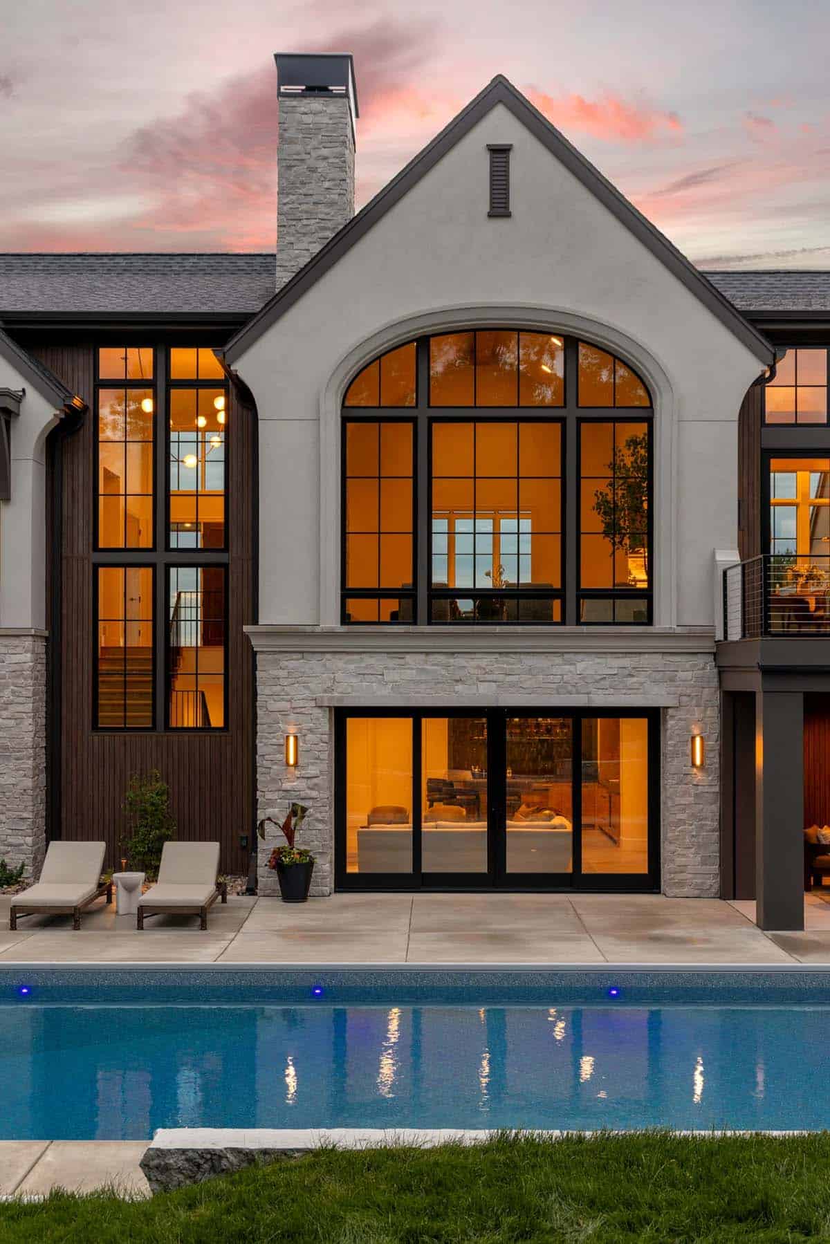 Arched window and stone chimney above pool-facing sliding doors at dusk