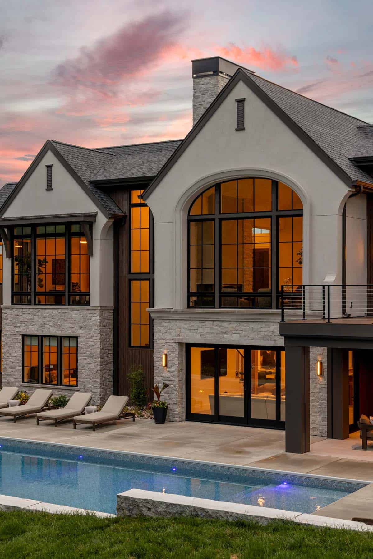 Stucco and stone rear facade with large arched window beside the pool