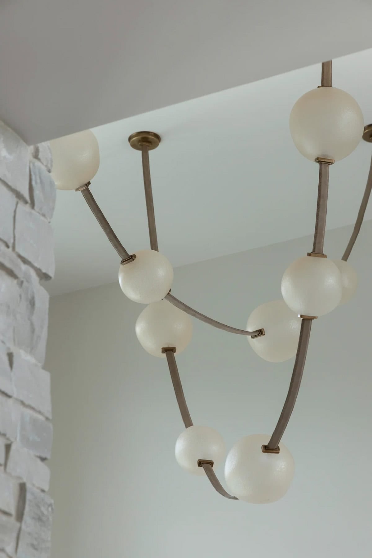 Sculptural chandelier with frosted glass globes and brass accents by stone wall