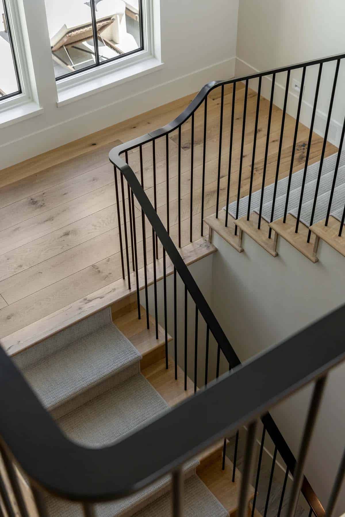 Staircase with black metal railing, wide plank floors, and carpeted runner