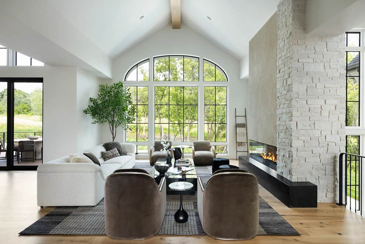 Vaulted living room with arched windows, stone fireplace, and velvet swivel chairs