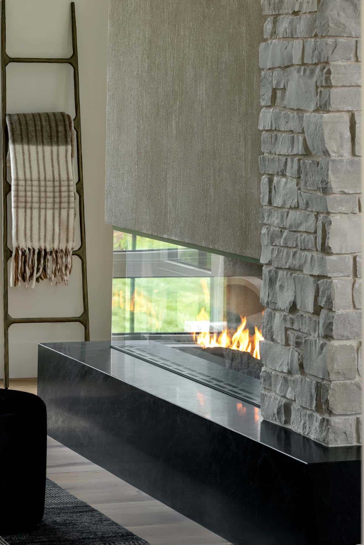 Glass corner fireplace with black stone hearth beside a blanket ladder